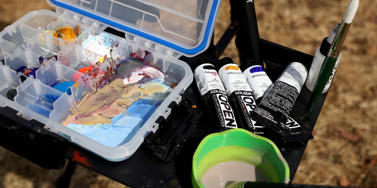 Flaconi e tubetti di acrilici Golden OPEN con campioni di colore sfumato su tavolozza, simbolo del loro tempo di asciugatura prolungato.